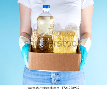 A girl in latex gloves holds a box of food for donations. Life-sustaining products. Products for a large family. Healthy diet. Cereals, oil, canned food.
