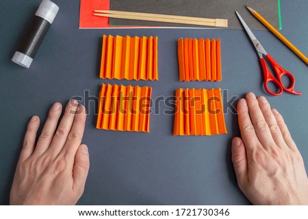 Paper Halloween Jack O'Lantern step-by-step instruction. Step 10: Four quarters of a folded sheet of orange paper lies in front of person. DIY Halloween decoration theme.