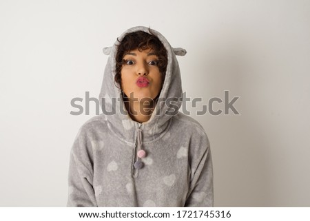 Pleasant looking young female female wearing pajama , keeps lips as going to kiss someone, has glad expression, grimace face. Standing outdoors. Beauty concept.