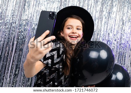young girl on holiday takes a photo on a smartphone among black balloons on a shiny background
