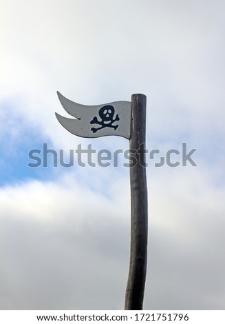 A Wooden Flag with a Skull and Crossbones or Jolly Roger on flying against a cloudy blue sky