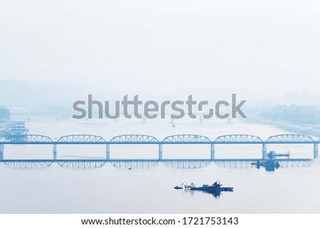 Pyongyang, DPR Korea. North Korea. Taedong bridge over Taedong River in the morning fog. View facing upstream from the Yanggakdo island Royalty-Free Stock Photo #1721753143