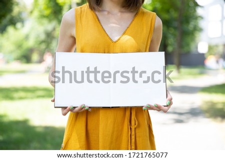 A girl keeps an open photo book with white paper on the street. Mockup for photo book design.
