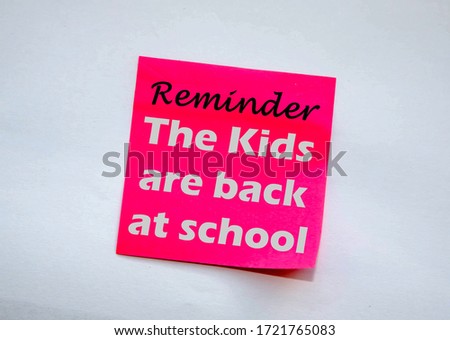 Pink note with the  message 'Reminder The kids are back at school on a grey wall as the rules are relaxed due to the Covid-19 pandemic's decline.  