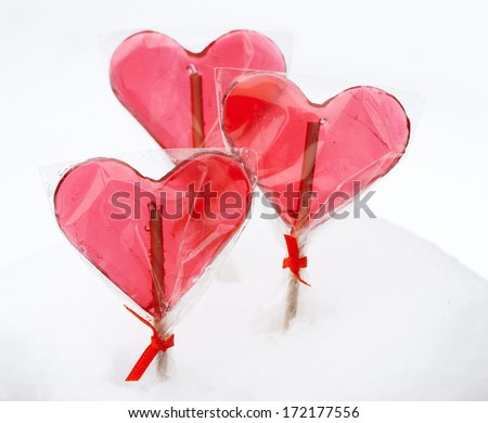 Heart shaped red lollipops on winter white snowy background close up. Valentine's Day concept.