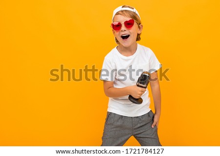 blond boy in glasses sings into a microphone on a yellow background