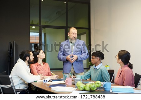 Senior businessman standing in front of his colleagues in board room sharing his ideas, copy space