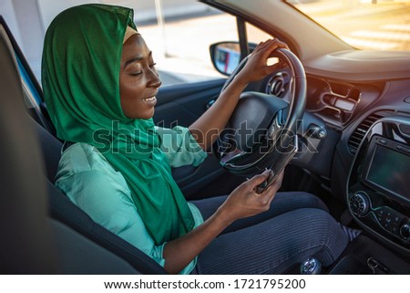 A young female driver watches the road as she drives with one hand. With the other, she texts on a smart phone. Woman driving car and texting message on smartphone