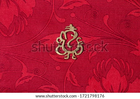 metallic lord ganesha symbol or icon on a beautiful red colored wedding card with beautiful patterns, lord ganesha face is of an elephant as per hindu mythology