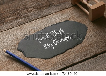 Selective focus of pencil,sand clock and a piece of torn black paper written with ' Small Steps Big Changes ' on wooden background.