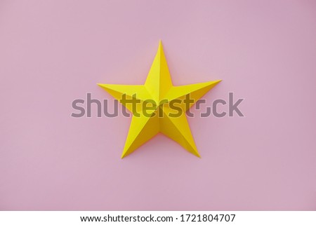 Handmade paper art and cut yellow star on pink background. Close up. 