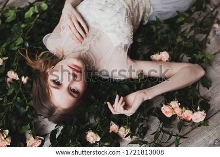Blonde bride in a fashionable wedding dress lies on a floor strewn with roses. Fashion wedding look concept
