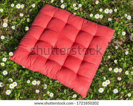 A red square cushion of fabric among the daisies of a meadow on a sunny day