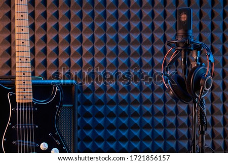 Electric guitar leaning on Guitar Amplifier Combo and microphone with professional headphones over acoustic foam panel background, with copy space between