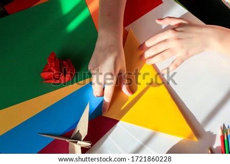Children’s hands doing origami crane from yellow paper on white background with various school supplies. Step-by-step tutorial of origami. Step 3. Concept of children's creativity, back to school.