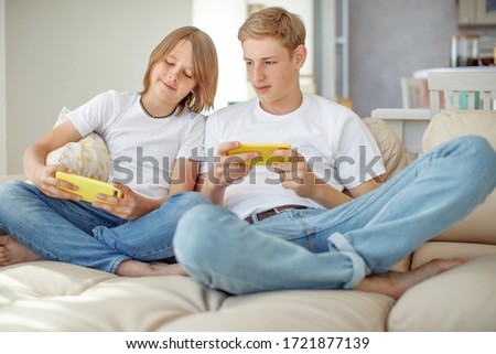 Teenagers play a game on the phone at home while sitting on the couch.
