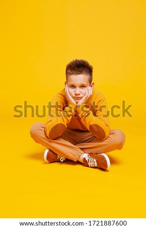 pensive teen boy sitting cross-legged. Photo taken on a yellow-orange background