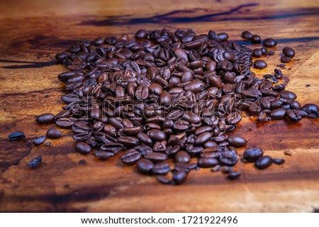 Macro photography of a heap fresh roasted coffee beans on a wooden background. High resolution detailed close up of brown roasted coffee beans on tropical wood table. Background  wallpaper image