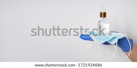 The hands of a doctor or nurse in blue latex protective gloves hold protective face masks and antiseptic: a place for text. Concept of infection control
