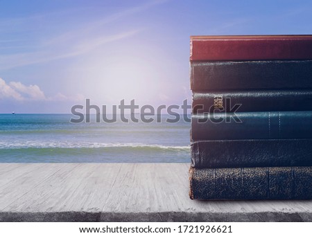 Stack of book and a holy bible on wooden table over sea and blue sky background Royalty-Free Stock Photo #1721926621