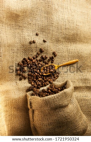 Burlap hessian sack of roasted coffee beans with wooden scoop on on factory texture background