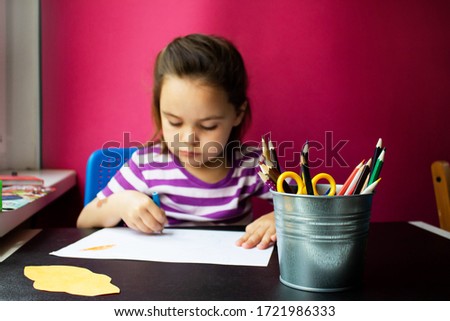 Cute child a girl of 4-5 years old draws is engaged in creativity. A small child sits at a Desk isolated against the pink background . Love family parenting the concept of childhood