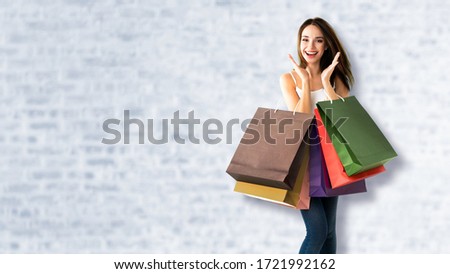 Shopping woman. Happy excited girl, holding bags, standing over white brick wall background. Copy space for some slogan, advertising or text. Consumerism and sales ad concept. 