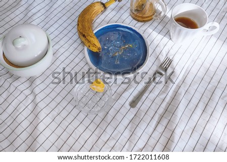 Crumbs and food object on table with blue ceramic plate and yellow banana on table with white clerical tablecloth. Stock photo.