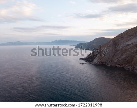 Aerial top view shot from drone. The speed boat rushes over the horizon on the vast Mediterranean sea among the majestic stone mountains and blue haze covering the sky. France, Port-Vendres.