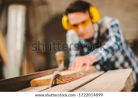 Professional carpenter using sawing machine for cutting wooden board at sawmill. Skilled cabinet maker working with electric circular saw at woodworking workshop. Man joiner, wood production workbench Royalty-Free Stock Photo #1722014899