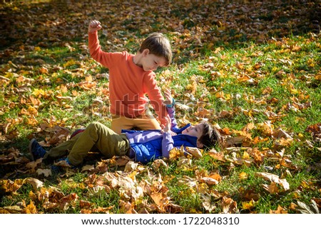Two boys fighting outdoors. Friends wrestling in summer park. Siblings rivalry. Aggressive kid hold younger boy on ground, try to hit him.