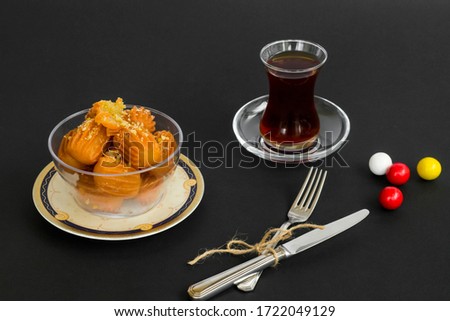 Traditional Turkish Crispy Dessert Tulumba,garnished with diced hazelnut in glass bowl on black with tea and cutlery set.The Sugar Feast Concept