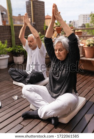 Vertical photo of a senior couple greeting God on the wooden terrace surrounded by plants
