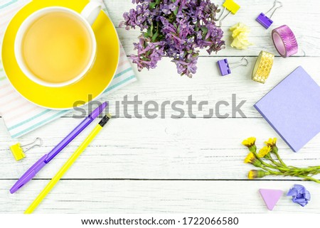 Business concept. Yellow Cup of tea on a saucer, lilac spring flowers, stationery, pen and pencil on a white wooden background. Space for text. Copy paste. Freelancing, working on the Internet.