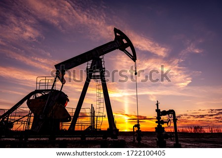 Oil Pumpjack against a sunset sky on background. industrial equipment. Rocking machines for power genertion. Extraction of oil. War on oil prices. Global coronavirus COVID 19 crisis.