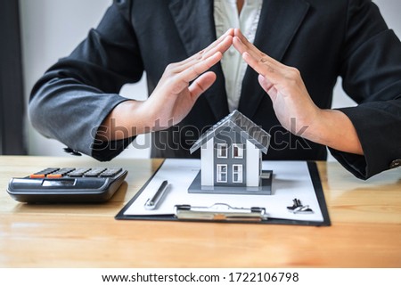 Real estate agent covering Small house model and protection by hands.