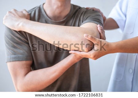 Doctor or Physiotherapist working examining treating injured arm of athlete male patient, stretching and exercise, Doing the Rehabilitation therapy pain in clinic. Royalty-Free Stock Photo #1722106831
