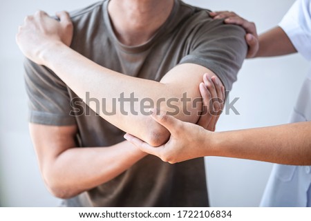 Female Physiotherapist working examining treating injured arm of athlete male patient, stretching and exercise, Doing the Rehabilitation therapy pain in clinic. Royalty-Free Stock Photo #1722106834