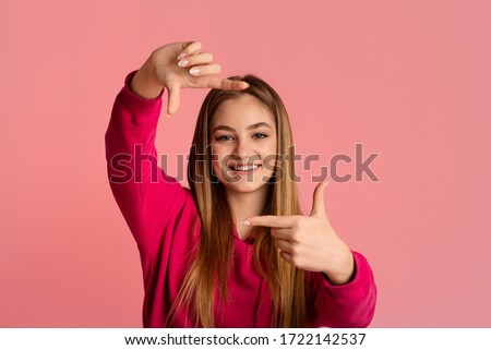 Smiling teenage girl makes photo with hands, empty space