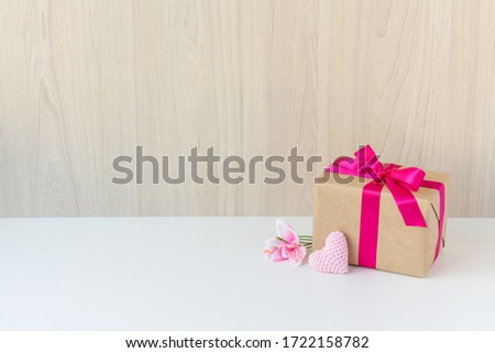 Happy Women's Day, Happy Mother's Day, Happy Valentine's Day and Happy Birthday. Have a flower, a crochet heart, a beautiful gift wrapped in a pink ribbon. Wooden background. White base. Copy space.