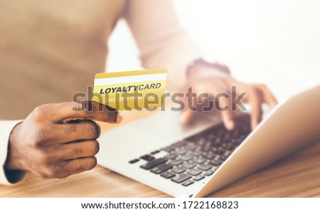 African American customer with loyalty card and laptop shopping via internet indoors, close up Royalty-Free Stock Photo #1722168823
