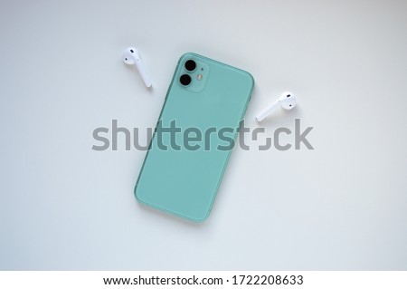 A modern mint-colored smartphone with two wireless headphones on the sides on a white background. Modern and minimalistic concept.