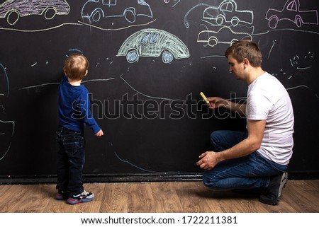little boy with dad draw chalk cars on a black slate wall. children's creativity. family leisure. the interior of the children's room.