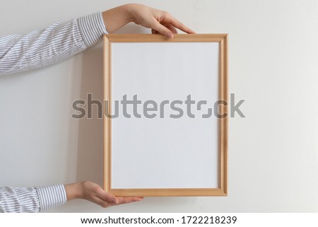 Cropped hand of woman holding picture frame against wall. Frame mock up.  Royalty-Free Stock Photo #1722218239