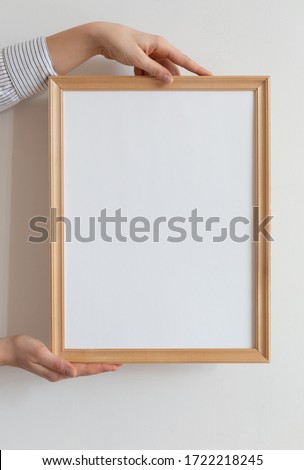 Cropped hand of woman holding picture frame against wall. Frame mock up. 