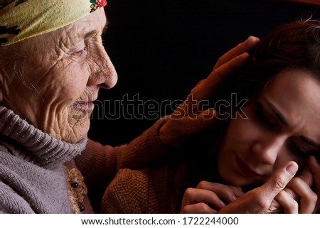 An old wrinkled hand of a grandmother strokes the hair of a young granddaughter. Caring grandmother spends time with her grandchildren close-up. Aged grandmother with wrinkles on her face blesses her 