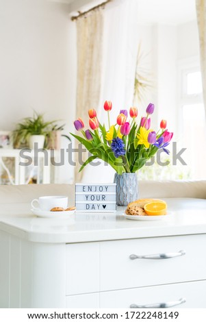Good morning concept. Romantic breakfast - fresh flowers, cup of hot drink, cookies, orange, lightbox with message Enjoy your day on marble table with light interior view. Vertical card. Copy space