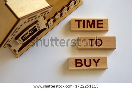 Wooden blocks form the words 'time to buy' near miniature house.