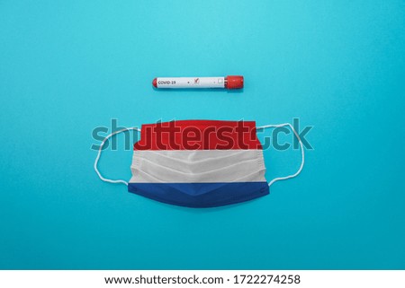 Disposable medical surgical face mask with Netherlands flag superimposed on it with positive COVID-19 test on blue background. Coronavirus (COVID-19) pandemic affects the country. Stay home, stay safe