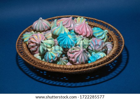 a sweet dessert in the form of multi-colored meringues on a blue background lies in a wicker basket on a tray.